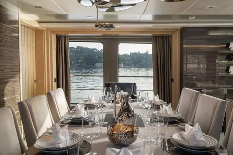 La sala da pranzo apparecchiata, coi bicchieri da vino e il mare dalle finestre
